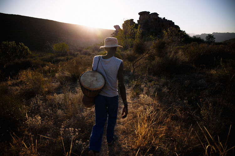 Rear view of man with drum walking on field during sunset