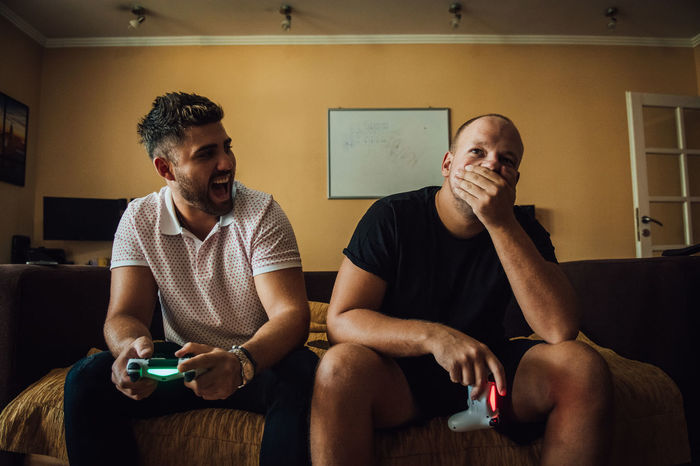 Man laughing on disappointed friend while playing video game at home