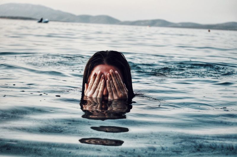 Woman covering eyes while swimming in sea