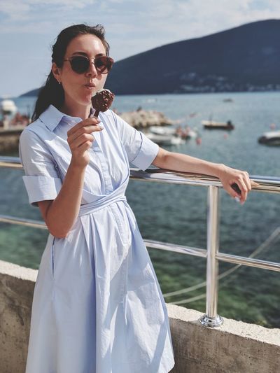 Woman eating ice cream while standing against sea