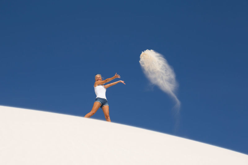 Low angle view of woman playing with sand against clear blue sky
