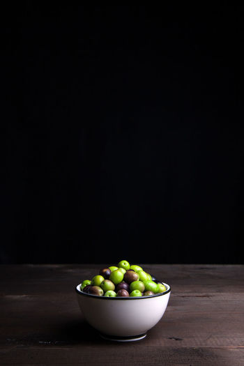 Close-up of green olives in bowl on table against black wall