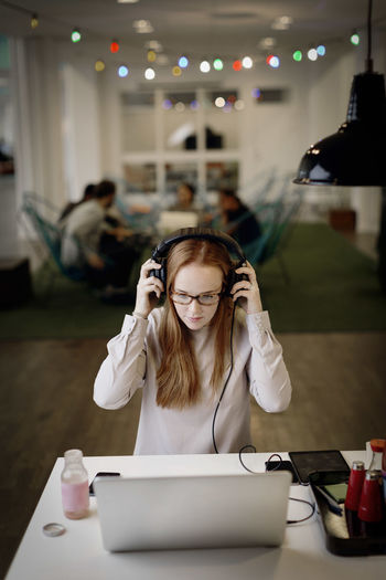 Businesswoman wearing headphones while working late on laptop in creative office