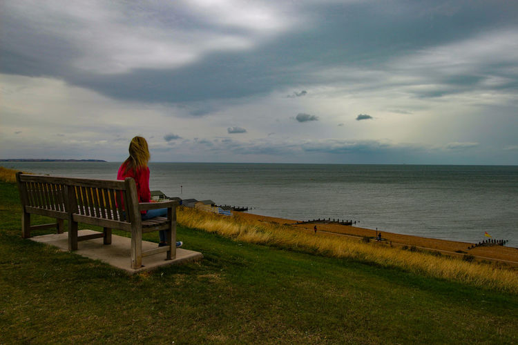 Man sitting on bench by sea against sky
