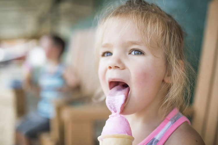 Young cute girl happily licking pink ice cream on summer day.