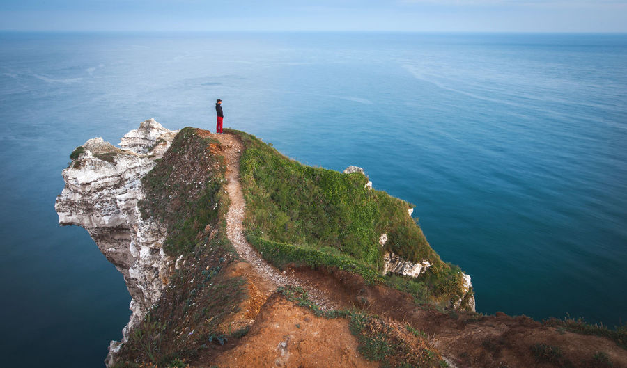 Mid distance view of man standing on cliff against sea