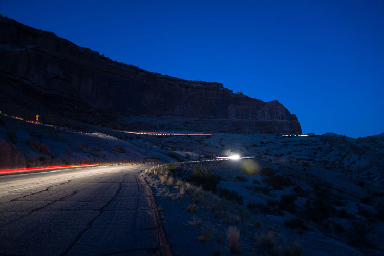Road by illuminated mountain against clear blue sky at night