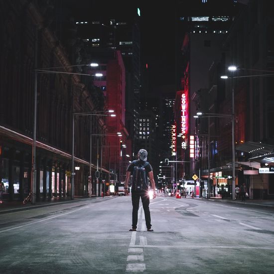 Rear view of man standing on street amidst buildings at night
