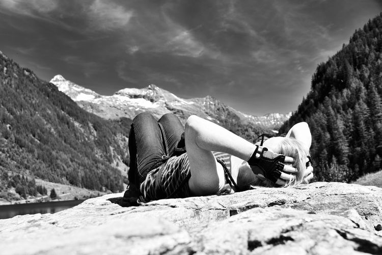 Woman lying on rock against sky