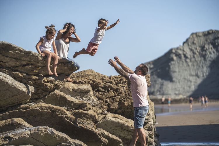 Carefree boy jumping onto father while mother and sister watching at beach