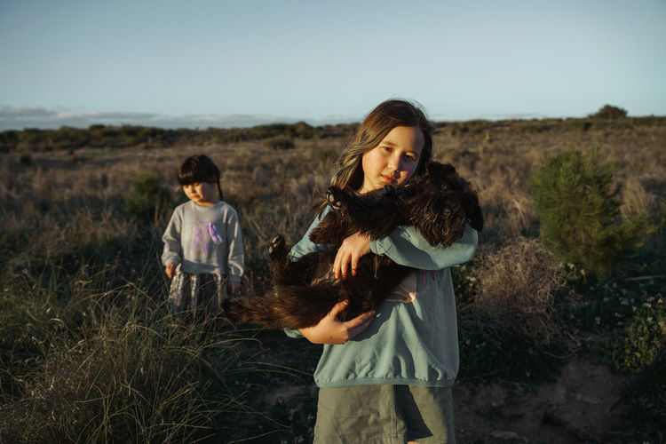 Side view of girl holding dog and  standing on field
