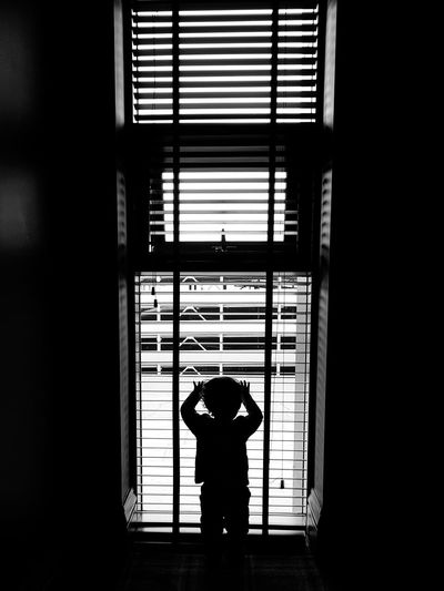 Rear view of silhouette boy standing by window