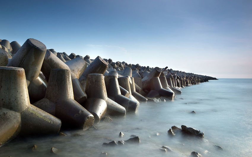 Tetrapods in sea against sky