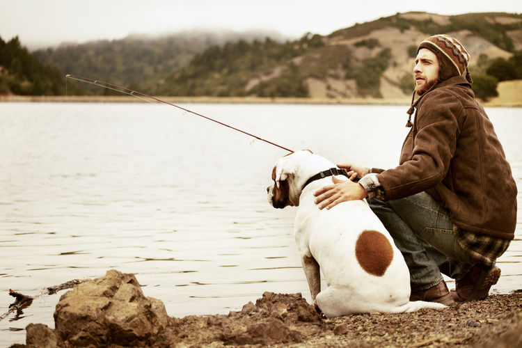 Traveler fishing while sitting with dog at lakeshore