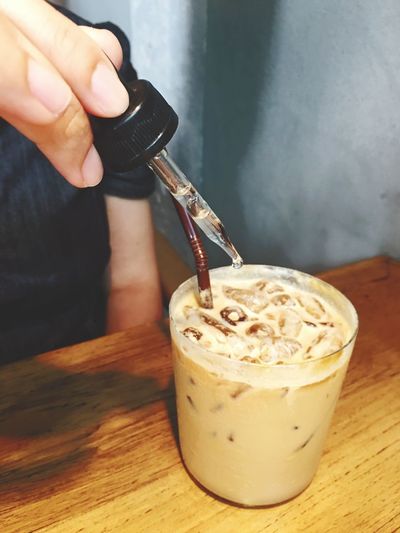 Cropped image of person adding liquid in iced coffee through dropper at restaurant