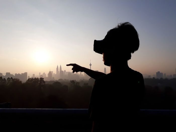Silhouette man wearing virtual reality against sky during sunset