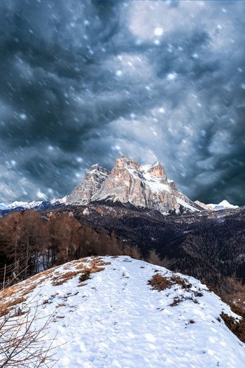 Scenic view of snowcapped mountain against cloudy sky during snowfall