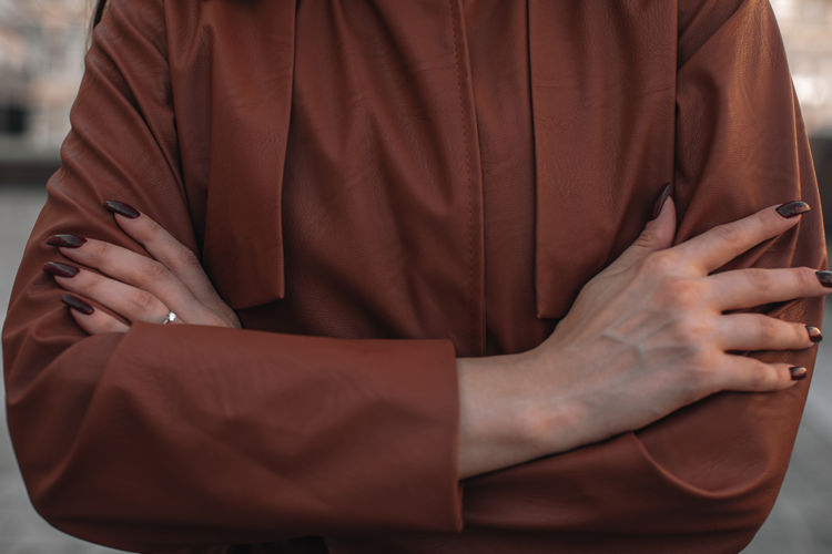 Street style fashion details of autumn trench leather coat. female hands with dark manicure.