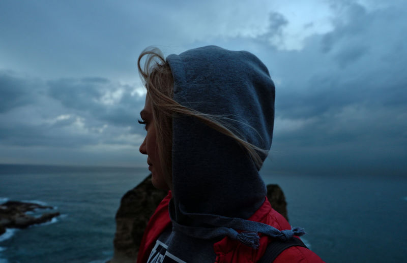 Side view of thoughtful woman looking at sea against cloudy sky