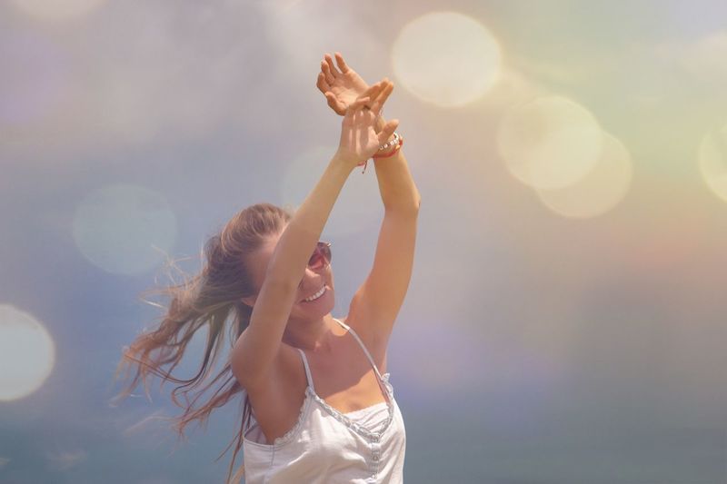 Woman with arms raised standing against sky on sunny day