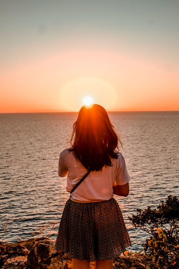 Rear view of woman standing at beach during sunset