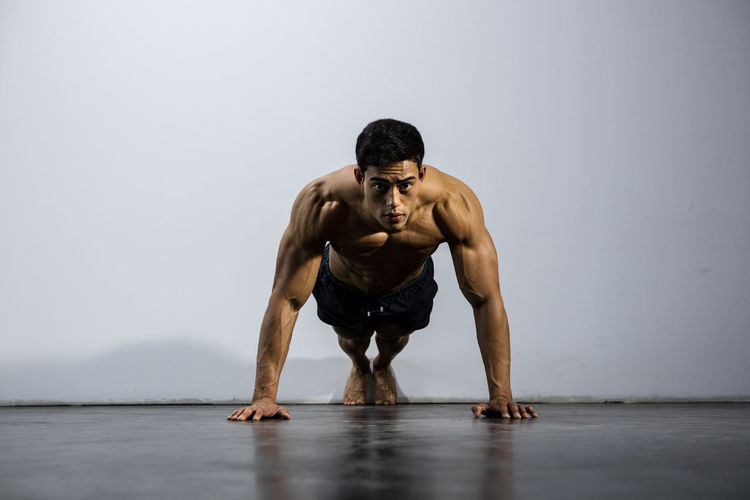 Portrait of shirtless man doing push-ups against wall
