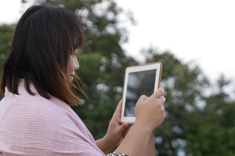 Woman using digital tablet against tree