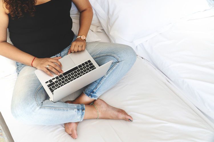 Midsection of woman using mobile phone while sitting on bed at home