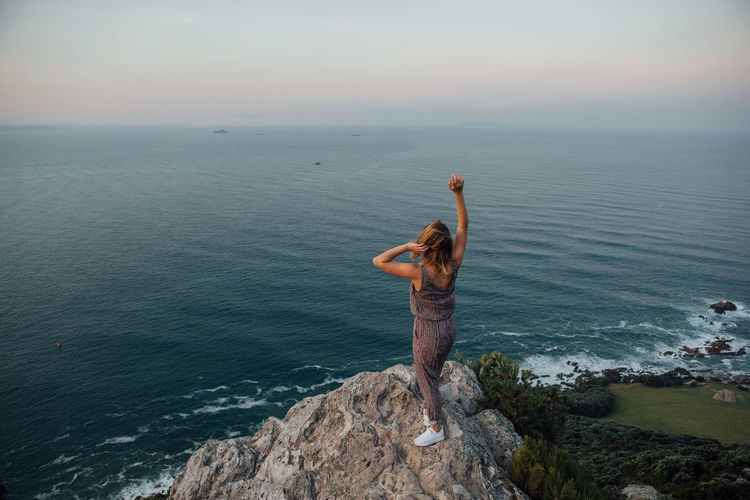 Rear view of young woman standing by sea against sky