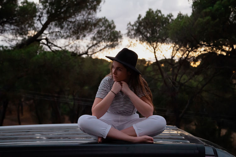 Full length of woman sitting against trees at park