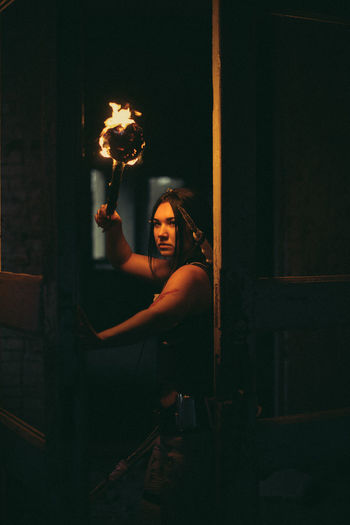Portrait of young woman holding torch in dark