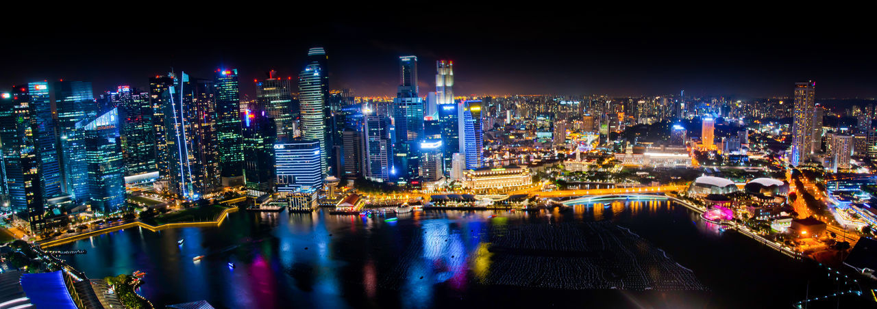 Illuminated buildings by river against sky at night