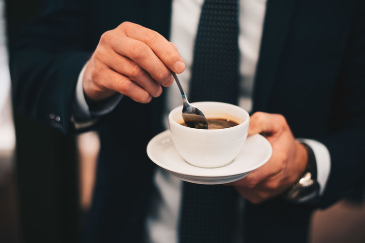 Midsection of businessman stirring coffee from spoon in cafe