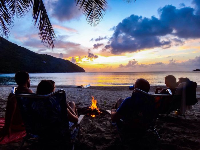 People sitting around bonfire on calm beach at dusk