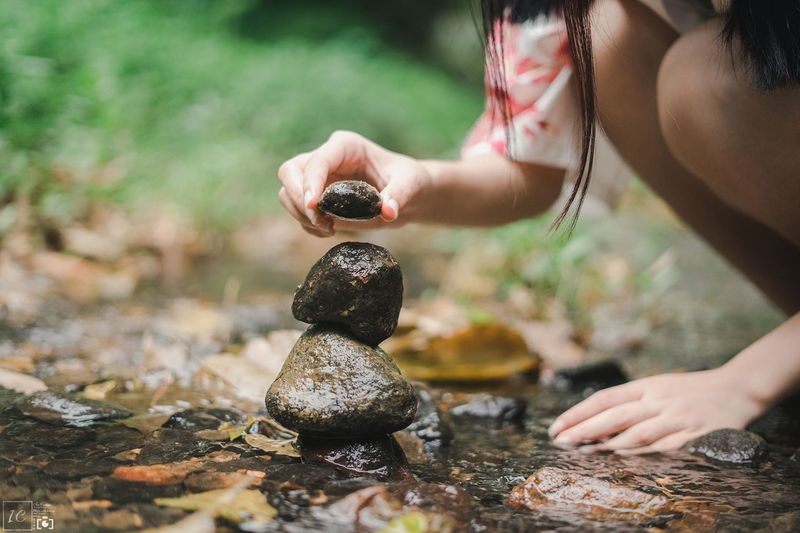 Cropped image of girl stacking stones on stream