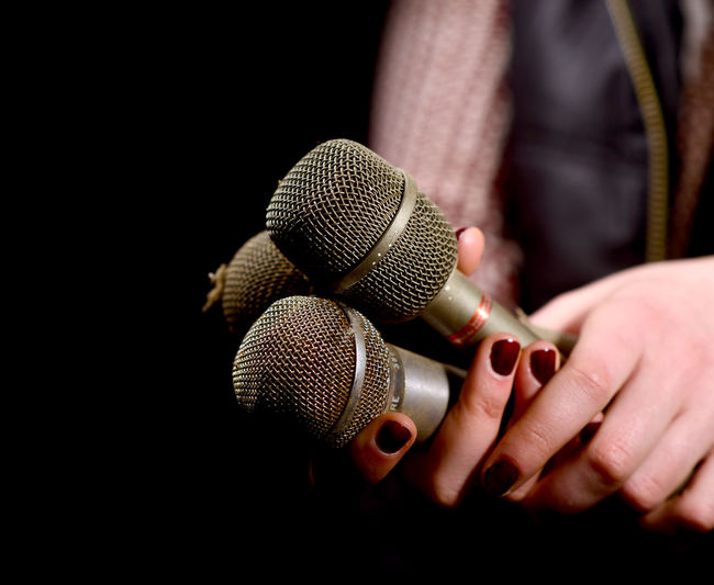 Cropped hands of woman holding microphones against black background