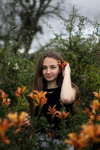 Portrait of smiling young woman wearing flower while standing amidst plants