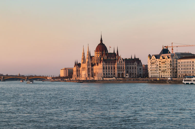 Hungarian parliament building by river against sky during sunset