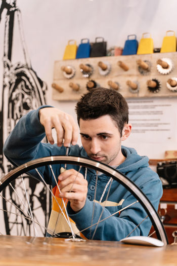 Serious male mechanic fixing wheel spoke while sitting at workbench in bike service