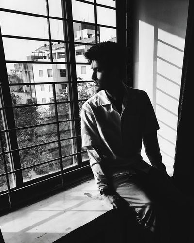 Young man sitting on window sill in apartment
