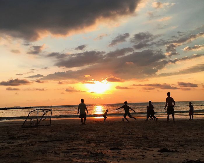 Silhouette males friends playing soccer at beach during sunset