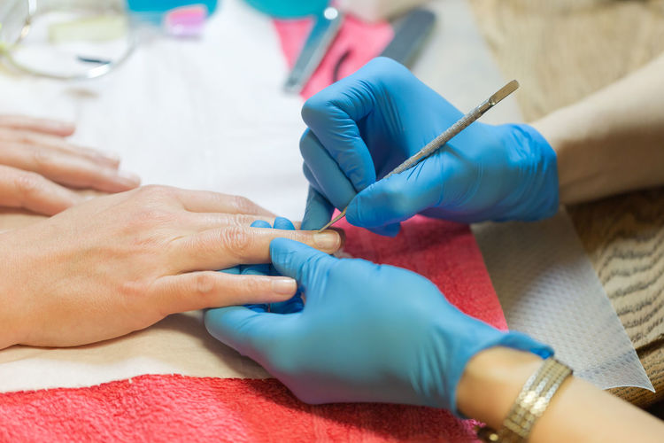 Self emplyed woman with blue sintetic gloves making manicure. close up focus on hands.