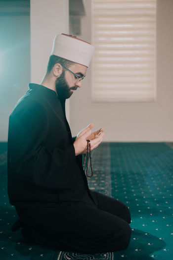 Side view of man praying while sitting in mosque