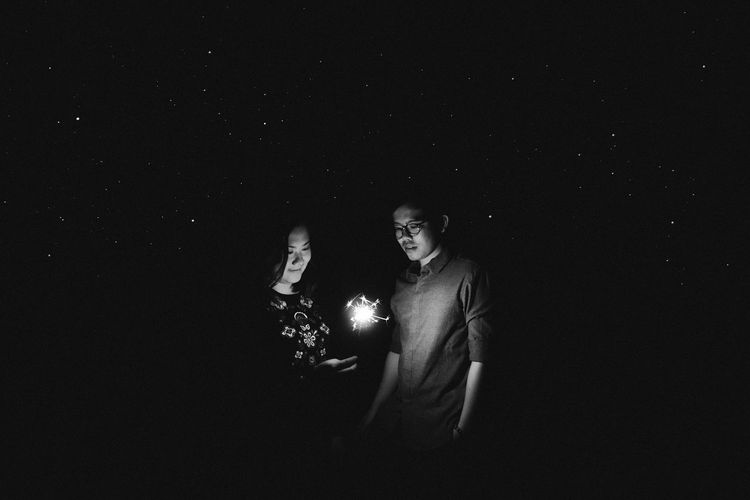 Friends burning sparkler against sky at night