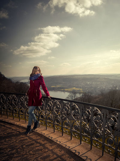 Woman standing on railing against sky