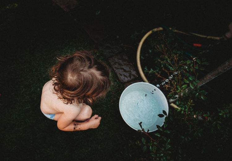 High angle view of shirtless girl sitting by bucket with water
