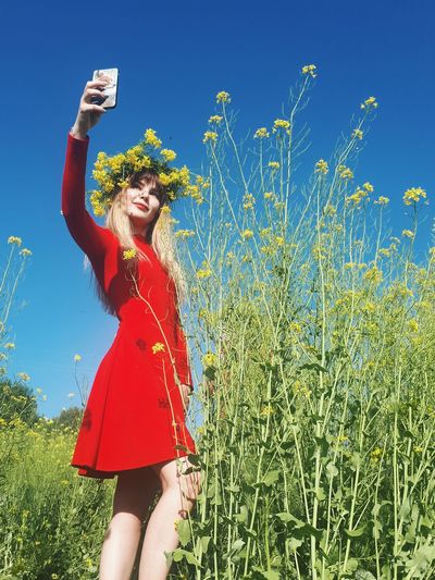 On a sunny day a woman in a red dress in a field of yellow flowers takes a selfie