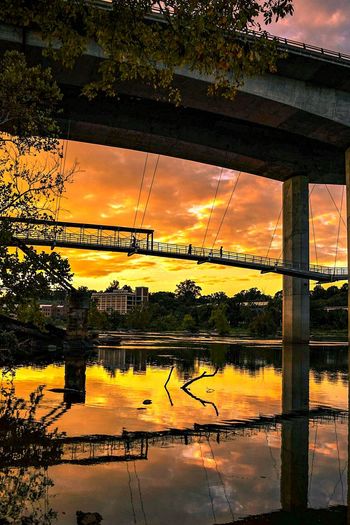 Reflection of trees on bridge against sky during sunset