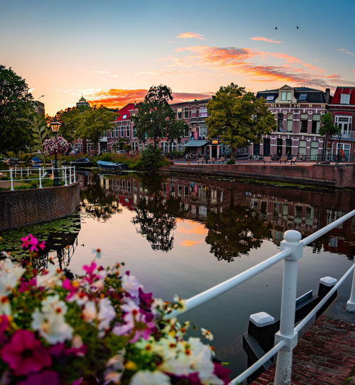 Scenic view of river by buildings against sky during sunset