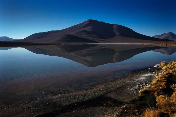 Scenic view of lake and mountains against clear blue sky